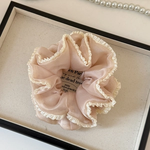 Detail of champagne organza scrunchie with pleated white lace edge on a tray