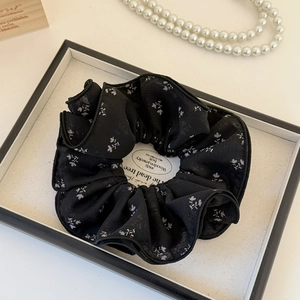 Détail d'un chouchou en maille noire à fleurs violettes sur un plateau élégant