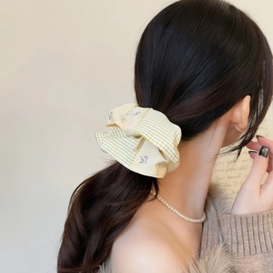 Close-up of yellow plaid and floral fabric scrunchie with a handmade label on a ponytail