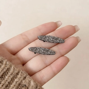 Close-up of small oval dark grey rhinestone hair clips on a soft beige background