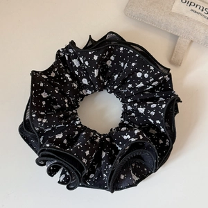 Macro shot of tiered black lace scrunchie with white floral patterns and layered mesh