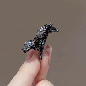 Barrette nœud noir ornée de strass brillants présentée en vue rapprochée à la main