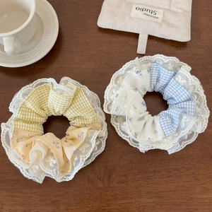 Close-up of yellow and blue plaid scrunchies with delicate white lace edges on wood
