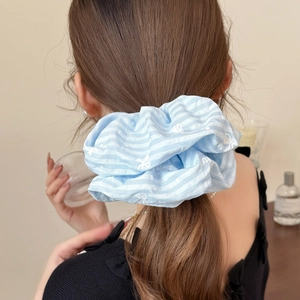 Blue and white striped scrunchie hair tie with white bow prints worn on a low ponytail