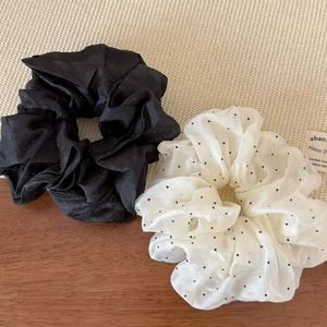 Detail of black and white polka dot organza hair scrunchies on a woven texture background