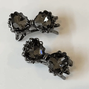 Détail de deux barrettes à nœuds gris foncé avec cristaux en forme de cœur sur fond blanc
