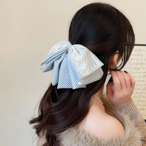 Close-up of blue plaid lace bow hair clip with pearl pendant on a girl's hairstyle