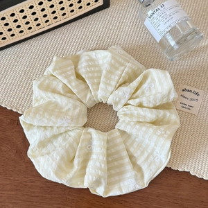 Detail of yellow checkered scrunchie with white butterfly embroidery on a textured mat