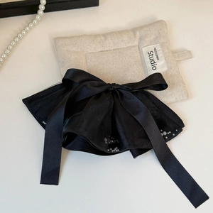 Detail of elegant black satin bow hair clip with white pearls and long ribbon tails