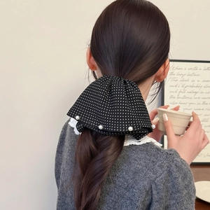 Detailed back view of a large black polka dot bow hair clip with pearls in a ponytail