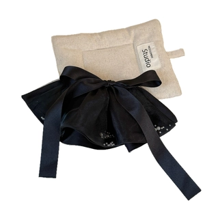 Elegant black satin bow hair clip with fine pearl trim on a textured display pad