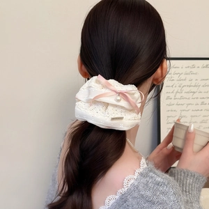 Détail du chouchou en dentelle avec nœud rose, perle et étiquette en métal