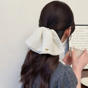 Detail of white polka dot chiffon bow hair clip with gold logo on model's ponytail