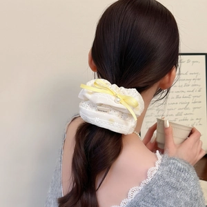 Détail de chouchou en dentelle blanche avec nœud jaune et perle sur queue de cheval