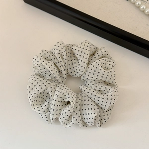 Dettaglio di un elastico per capelli in rete bianca a pois neri su fondo bianco