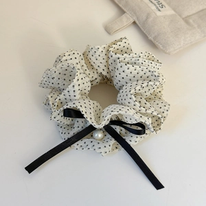 Close-up of cream polka dot scrunchie with a black ribbon bow and elegant pearl charm