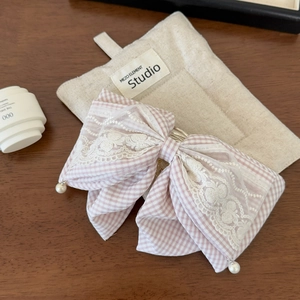 Close-up of pink plaid bow hair clip with white lace embroidery and pearl pendants