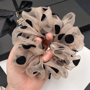 Détail d'un chouchou en maille abricot à pois noirs en velours tenu dans la main
