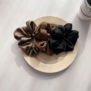 Three satin scrunchies in coffee, brown, and black on a ceramic plate detail