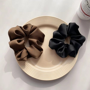Detailed texture of large matte satin scrunchies in coffee and black on a ceramic plate