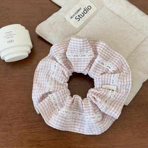 Close-up of pink plaid scrunchie with lace trim and Hand Made label on wood surface