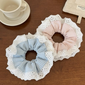 Close-up of pink and blue plaid scrunchies with white lace edges on a wooden table