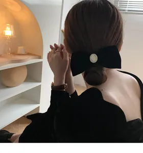Elegant black velvet bow hair clip with oval pearl center worn by a model in soft light