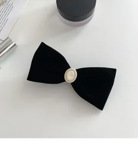Detail of elegant black velvet bow hair clip with faux pearl and gold bead accents