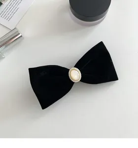 Detail of elegant black velvet bow hair clip with oval pearl centerpiece and gold bead trim
