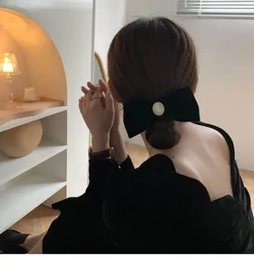 Detailed view of a large black velvet bow hair clip with a pearl center on a low ponytail