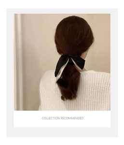 Detail of double-layered bow hair tie with white piping on beige knit sweater background