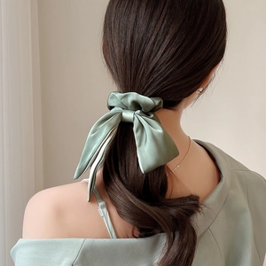 Detail of elegant sage green silk satin bow hair scrunchie worn on a low ponytail