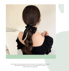 Detail of elegant black satin bow hair tie with long ribbons on a model's ponytail
