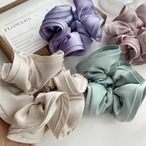 Vue détaillée de quatre chouchous en satin plissés de différentes couleurs sur fond blanc