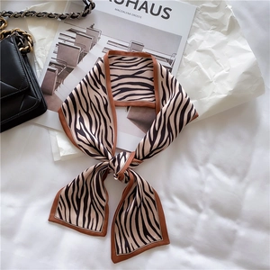 Detail of zebra print silk ribbon scarf with brown borders tied on a black quilted bag