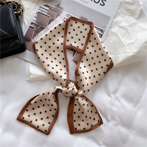 Close-up of vintage beige polka dot silk twilly scarf tied in a bow with black quilted handbag