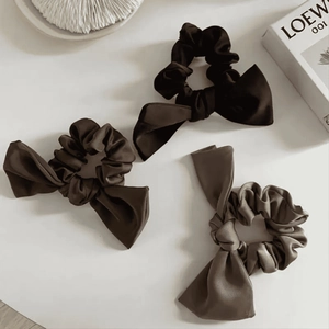 Three elegant satin bow scrunchies in black and brown displayed on a minimalist background
