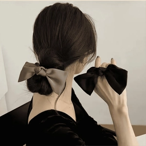 Detail view of smooth black and brown satin bow hair ties on model's hand and hair