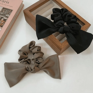 Detail of elegant black and dark brown satin oversized bow scrunchies on wooden box