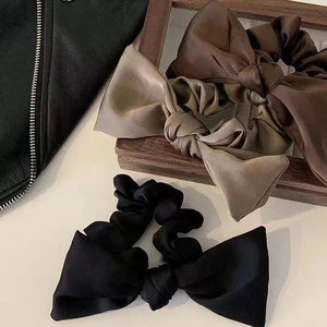 Three satin bow scrunchies in black, brown, and khaki displayed on a wood frame