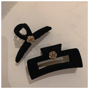Detail view of black velvet hair claws with gold camellia flowers on a stone background