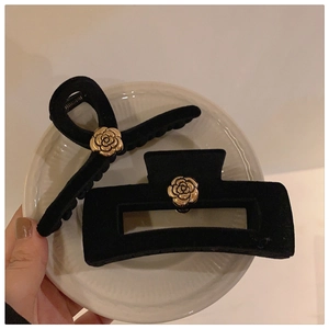 Detail view of black velvet hair clips with golden camellia floral embellishments