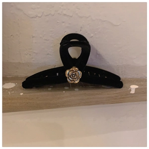 Detail of black velvet hair claw clip featuring a 3D gold rose on a textured background