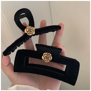 Detailed view of black velvet hair claws featuring gold camellia flower accents