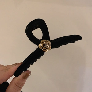 Detailed macro view of black velvet hair claw clip with golden camellia flower accent