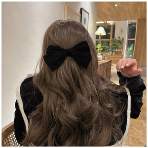 Macro shot of large black velvet bow hair clip worn on long brown wavy hair