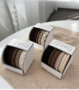 Trois boîtes d'élastiques à cheveux tressés aux tons terre sur un tapis en tricot