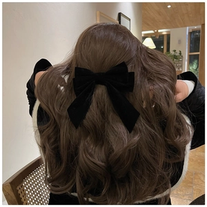 Detail view of a large black velvet bow hair clip styled on elegant long wavy hair