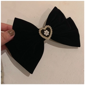 Detail of a large black velvet bow hair clip with a gold-edged heart and camellia flower