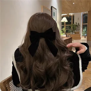 Elegant large black velvet bow hair clip worn on long brunette wavy hair in a cozy cafe